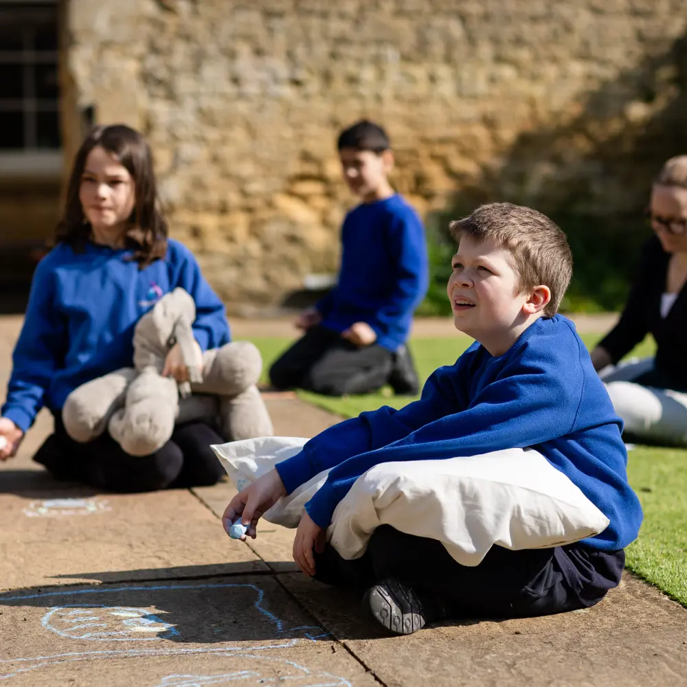 Three children and one teacher from Chilworth House School sat on the floor outside playing with chalk