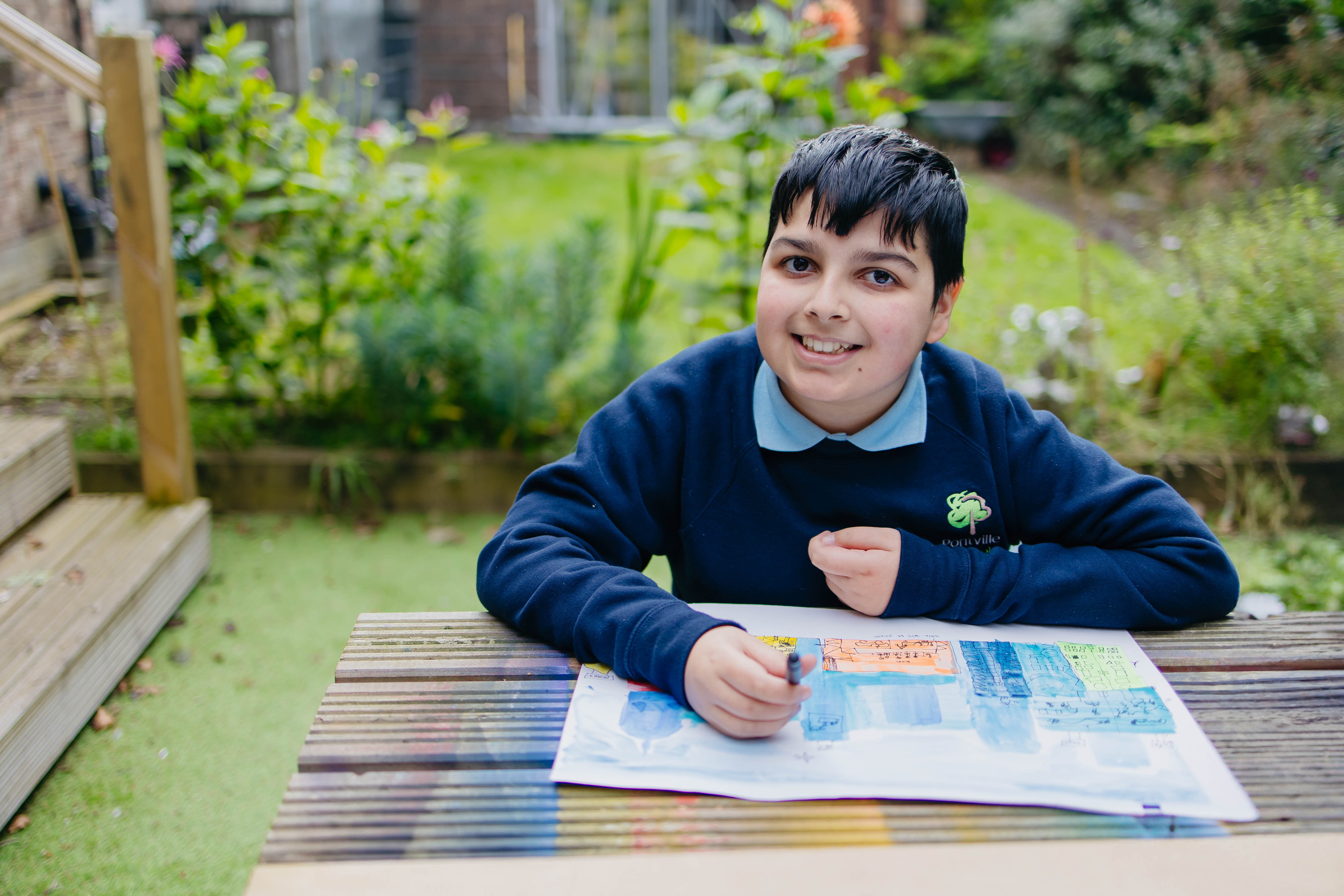 Young boy from Pontville School sat in school gardens colouring at a bench 