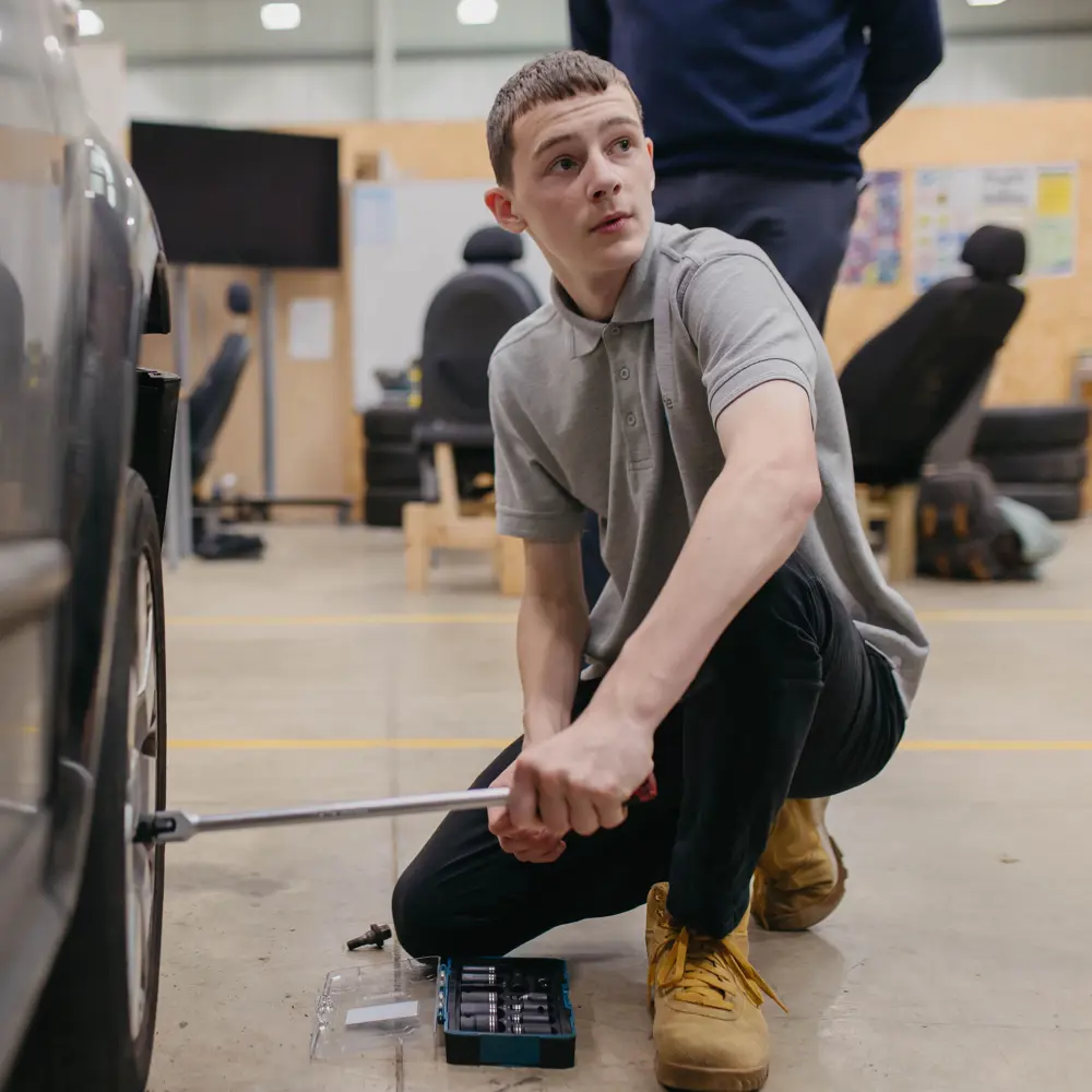 A boy changing a wheel on a car in a garage