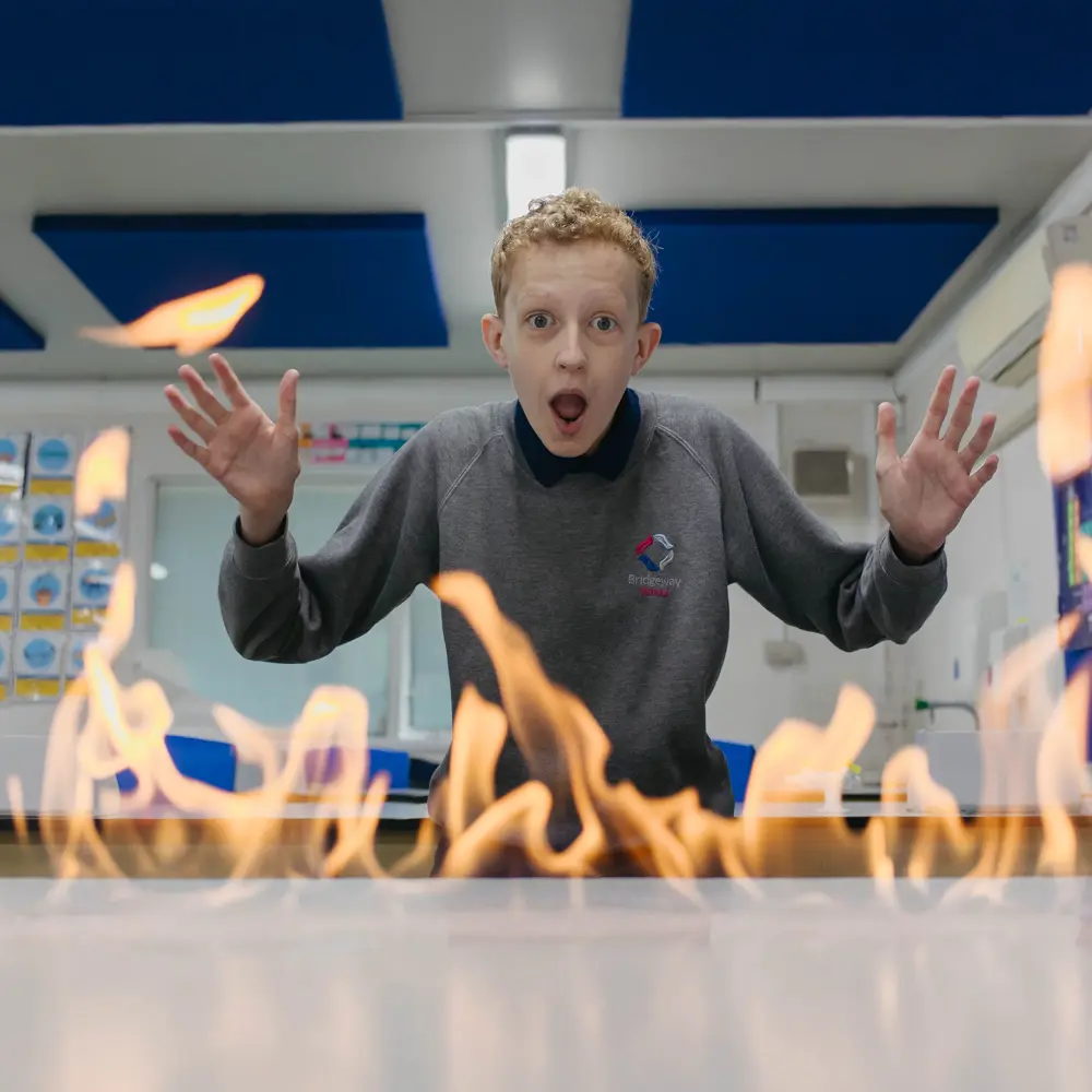 A young boy with ginger hair looking shocked at a row of flames in a science lab