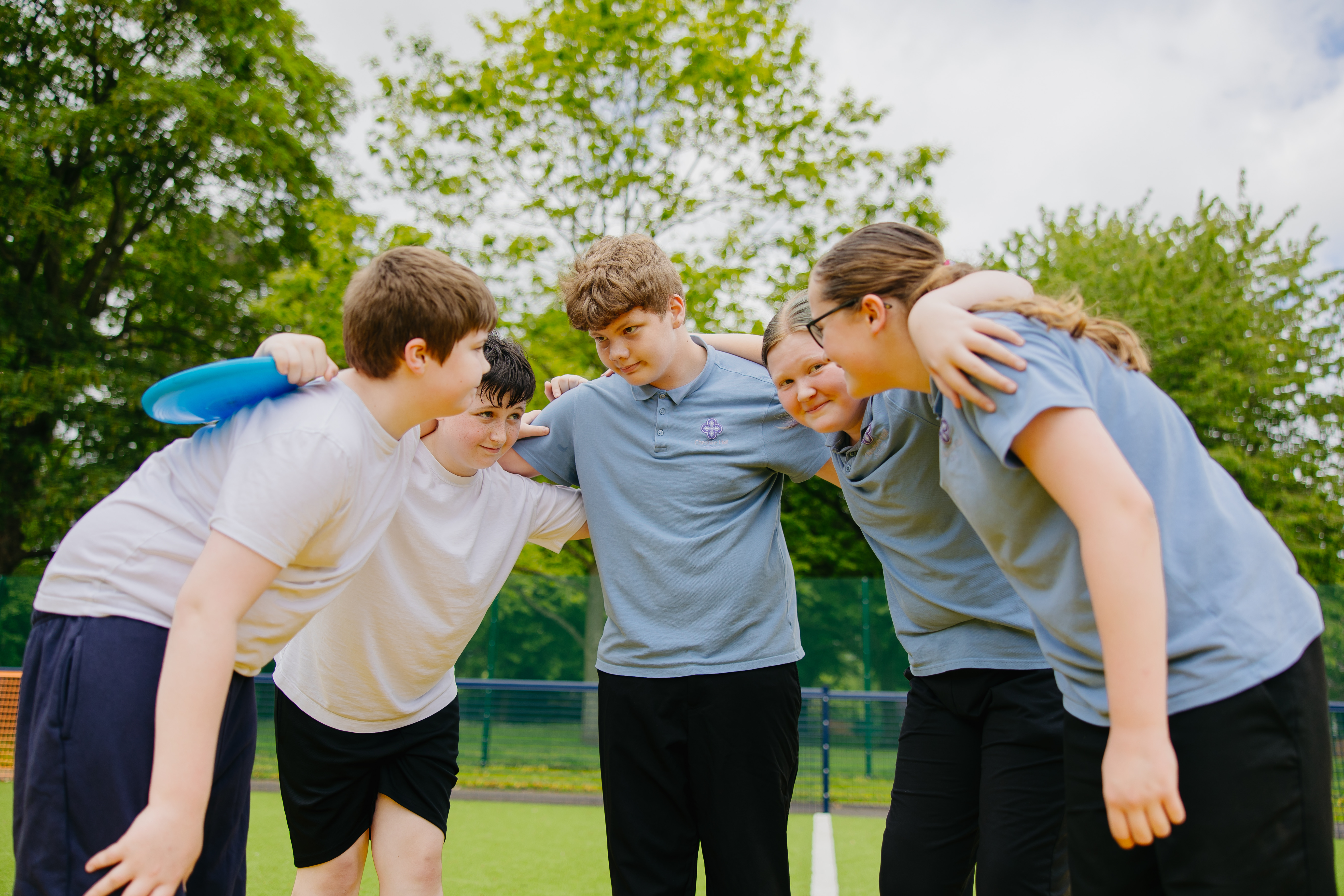 Five pupils stood in a circle with arms round eachother smiling