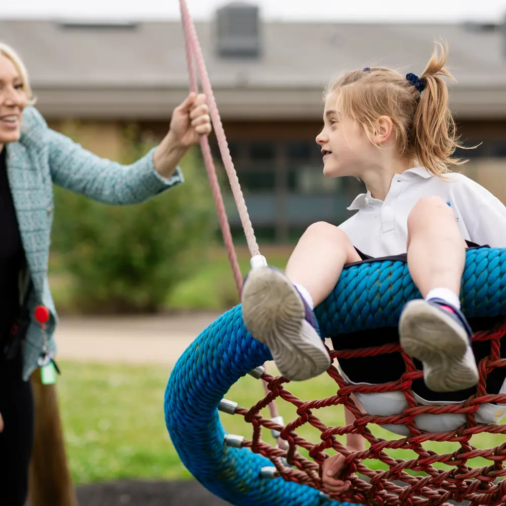 Young girl from Luxborough Court School swinging on a basked swing and being pushed by a member of staff