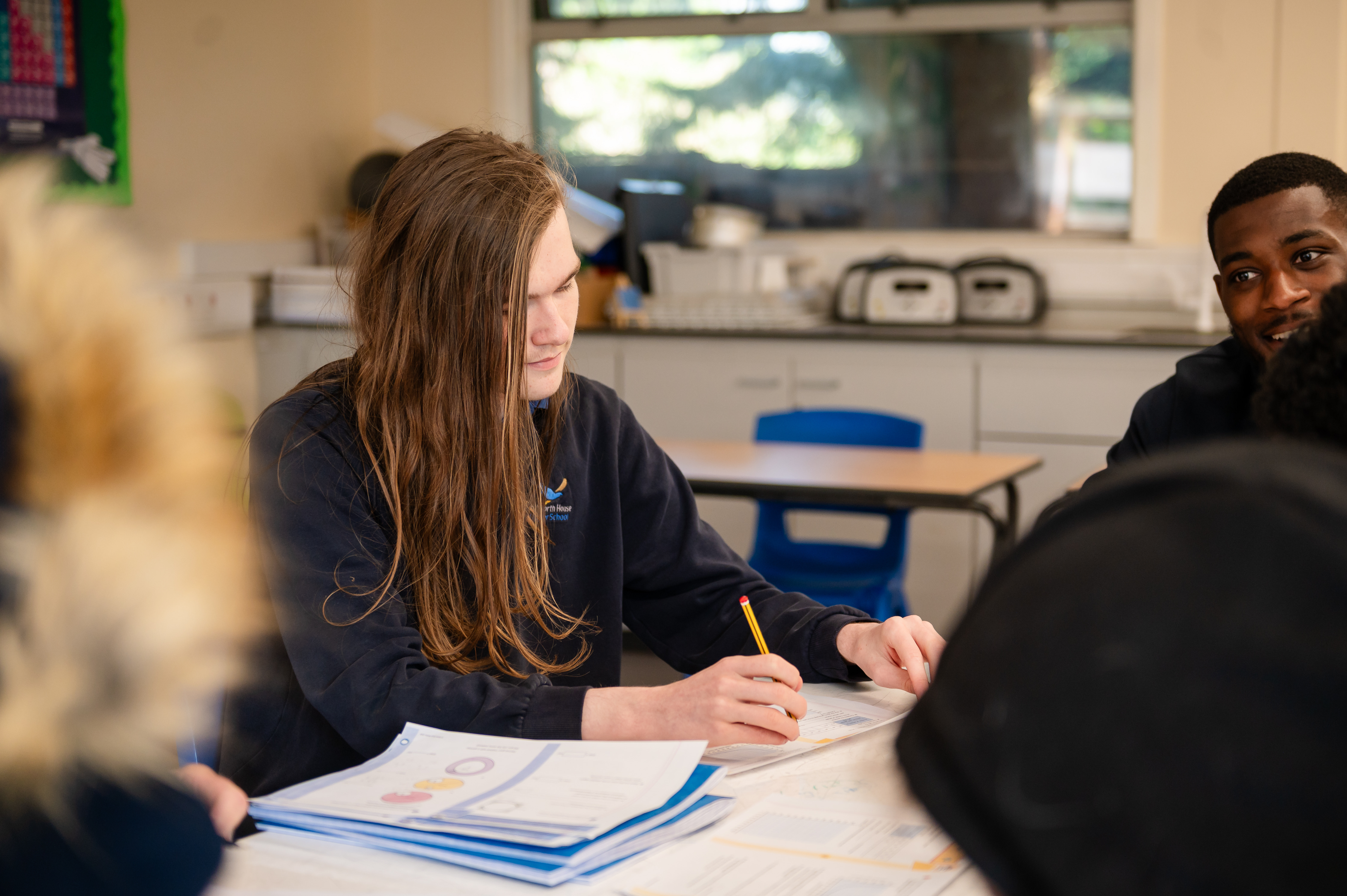 Boy with long brown hair sat at desk focusing on school worksheets