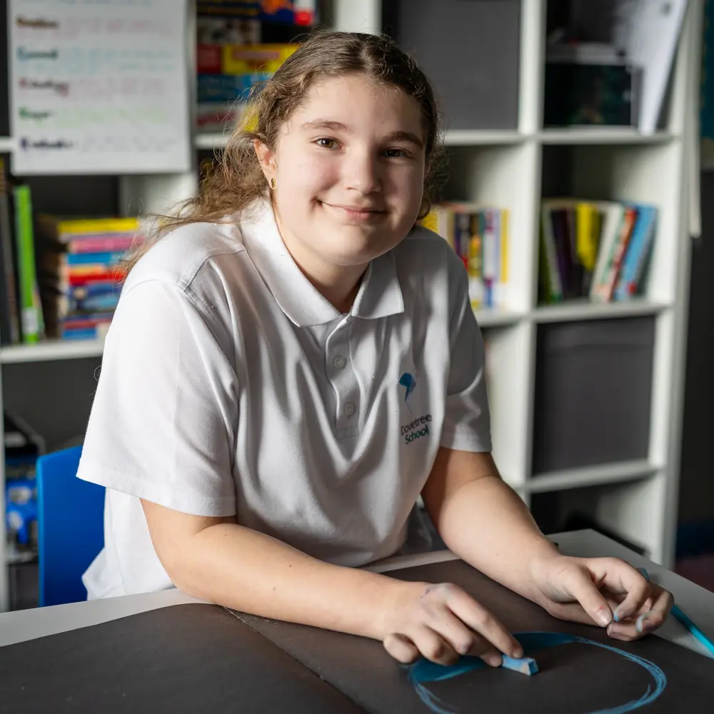 A young girl at Dovetree School working in a classroom smiling at the camera