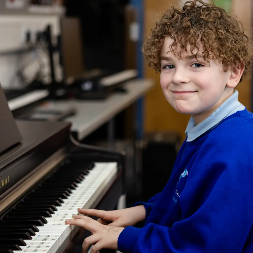 A young boy at Dovetree School playing the piano smiling at the camera