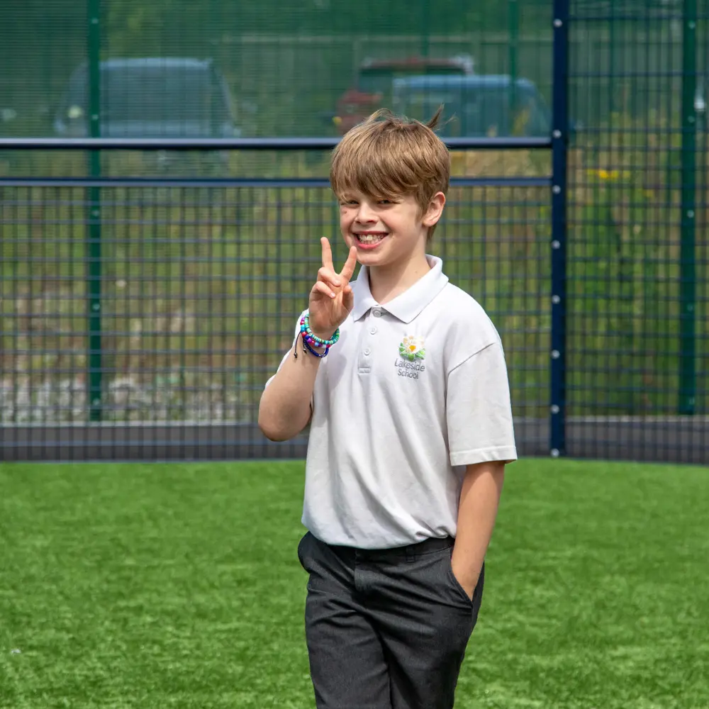 A young boy at Lakeside School smiling doing a peace sign at the camera