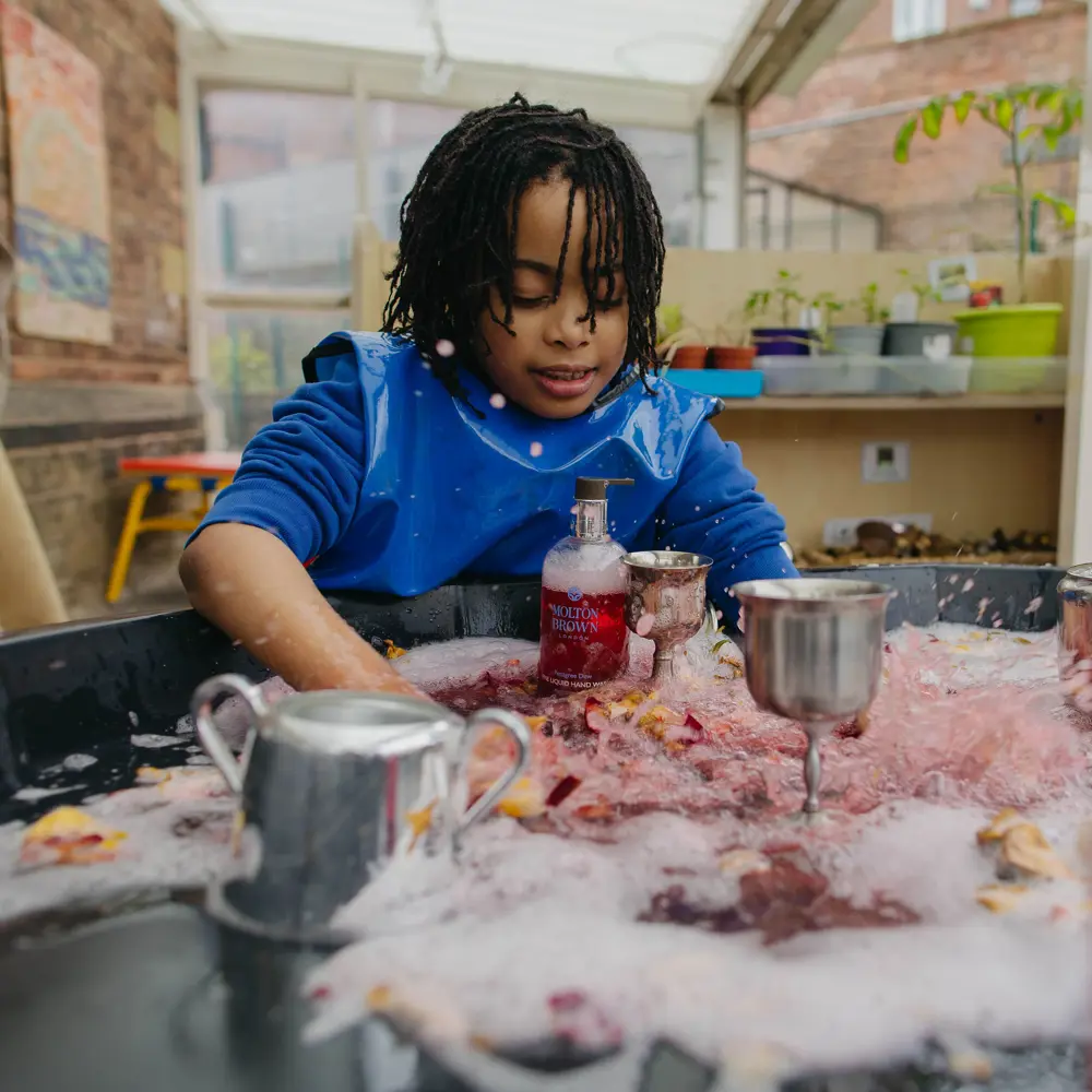 A young boy at Westmorland School playing with at a sensory table wearing an apron