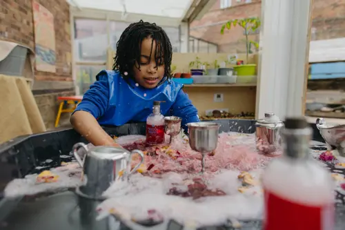A young boy at Westmorland School playing with at a sensory table wearing an apron