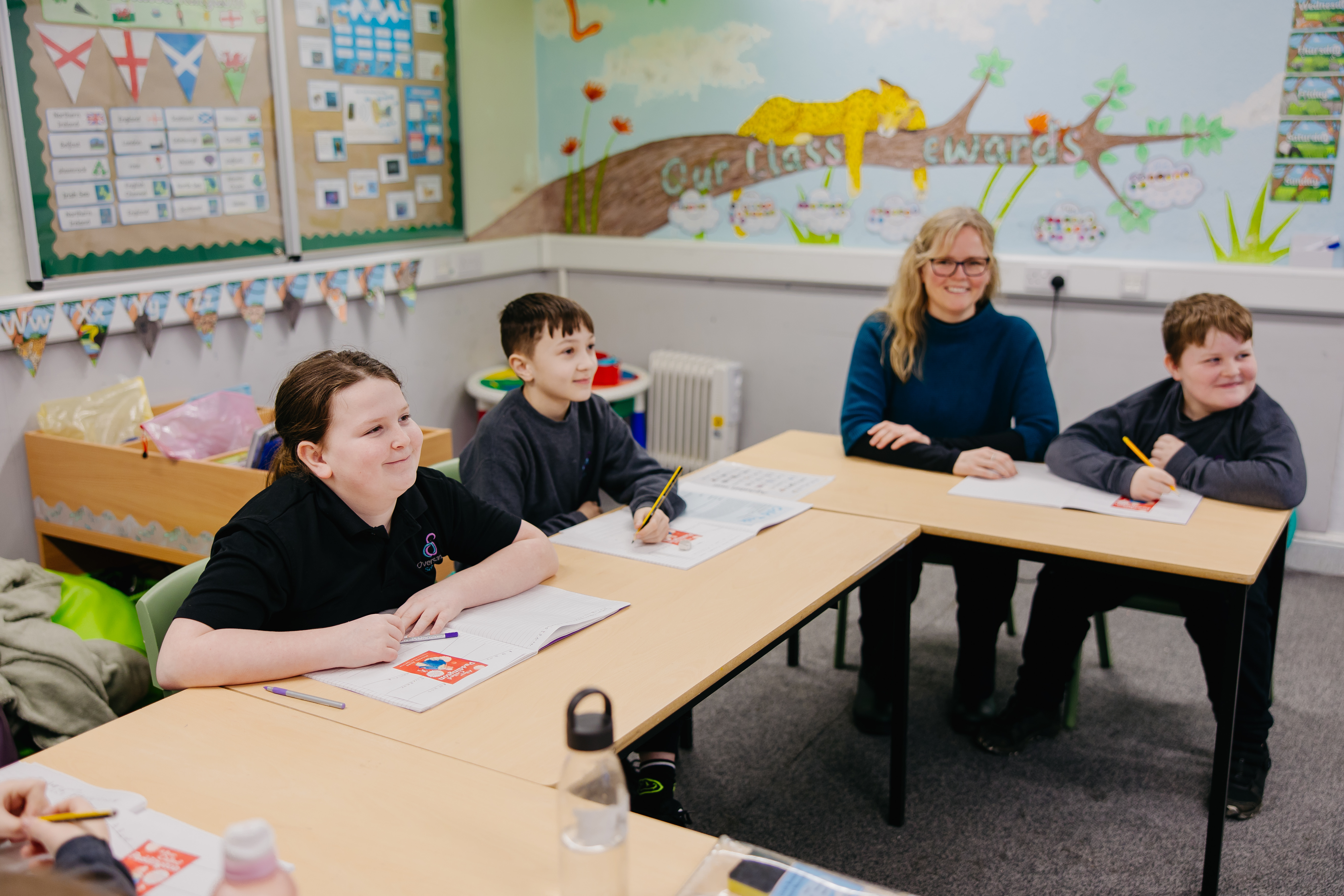Three pupils and a teacher sat as school desks learning