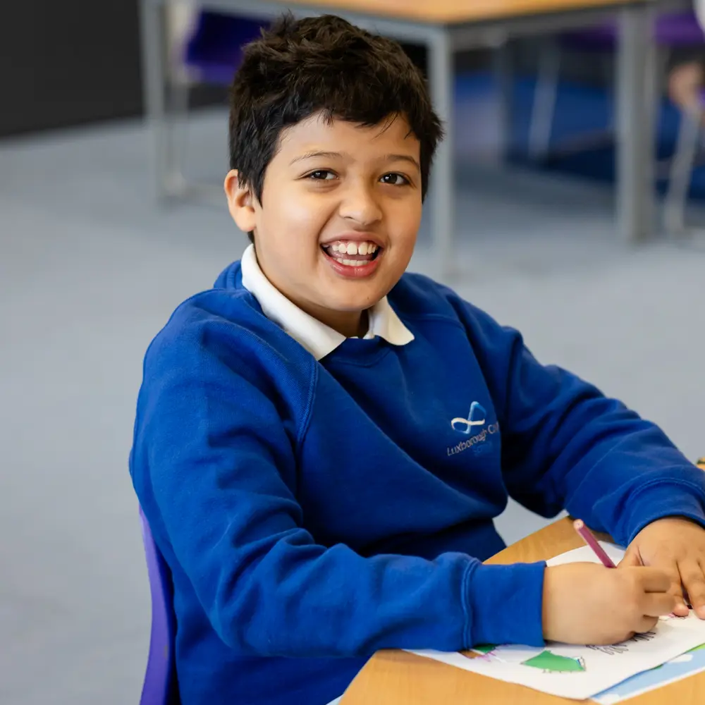 A young boy with brown hair at Luxborough Court School sitting at a desk doing his school work