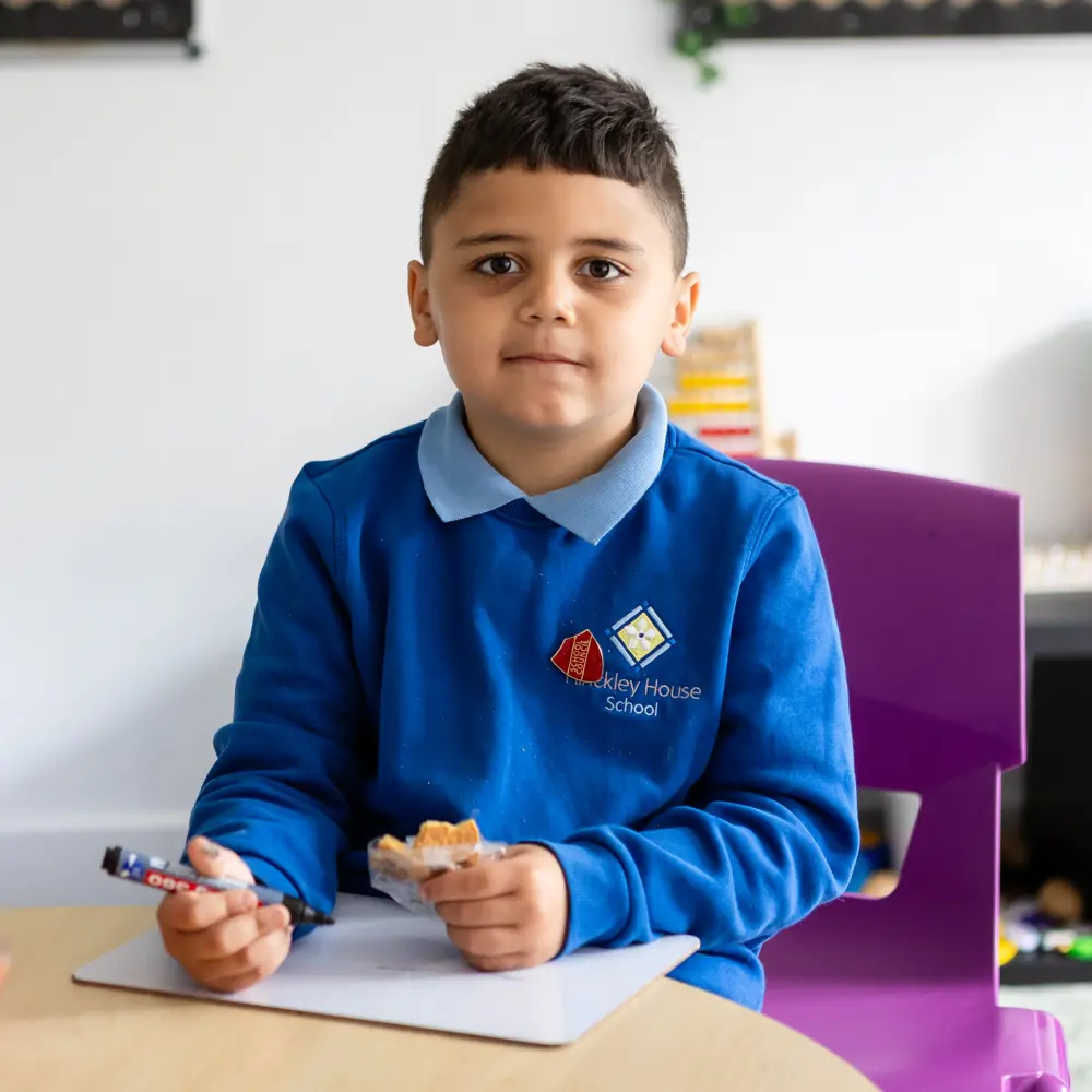 Young boy with brown hair holding a pen in one hand and a snack in the other while looking at the camera