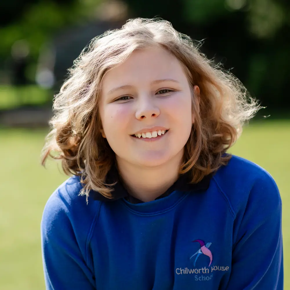 Young child from Chilworth House School with blonde curly hair sat outside smiling into camera