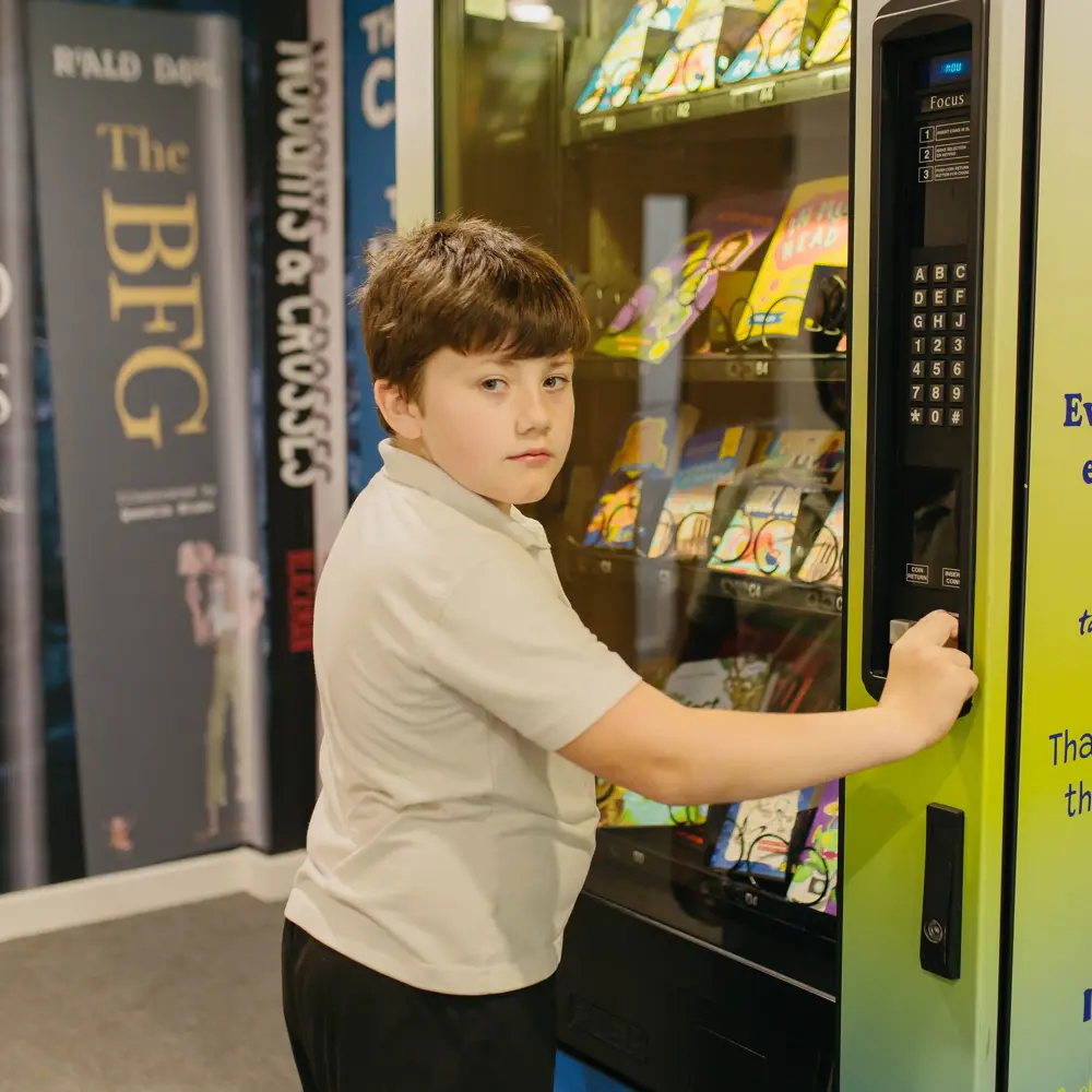 Young boy stood by book vending machine at Hartwell School