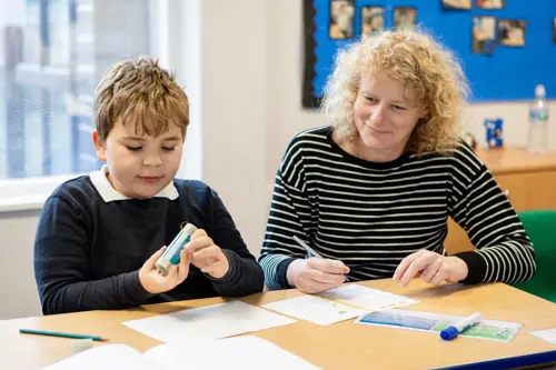 A young boy with blond hair at Queensmead House School working with a member of staff