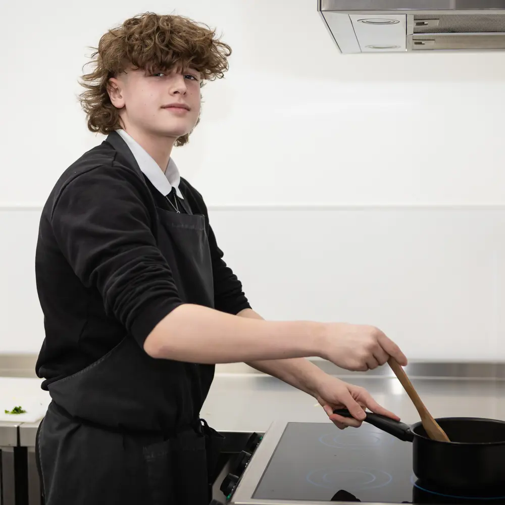 A young boy at Dovetree School cooking in a food technology class smiling at the camera