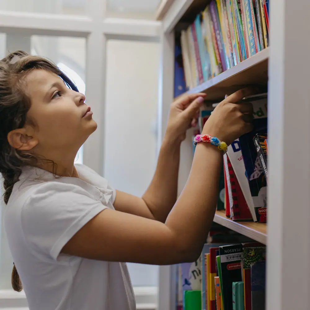 A young girl choosing a book from a bookshelf at Hall Cliffe Primary School