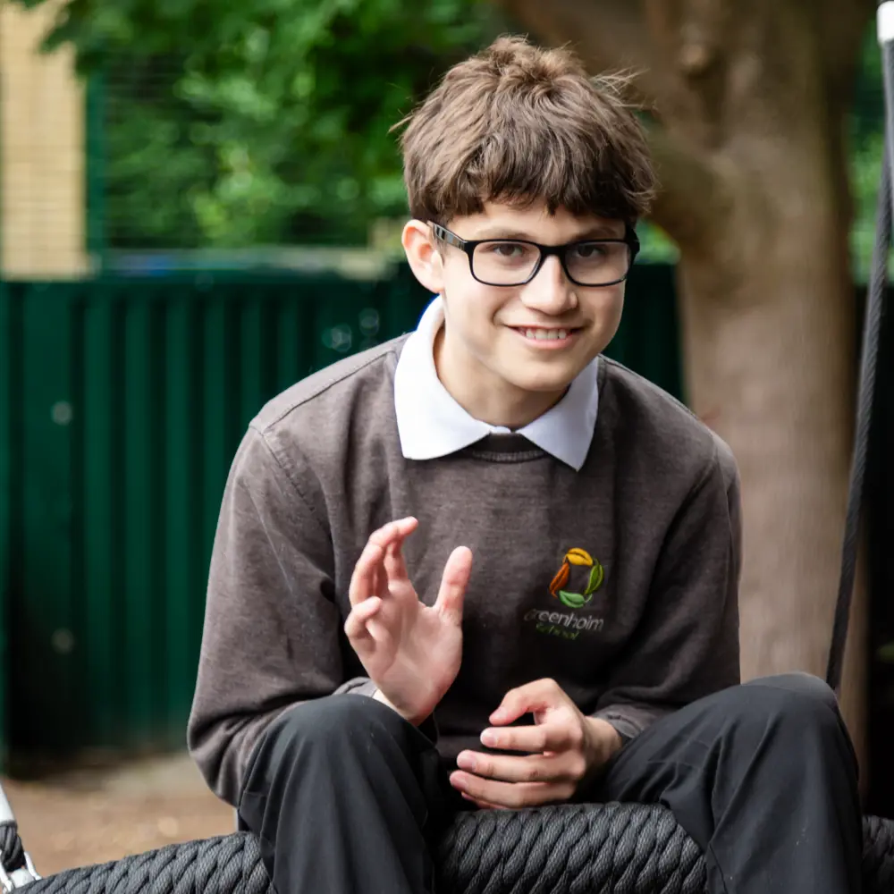 A young boy at Greenholm School smiling and waving at the camera outside