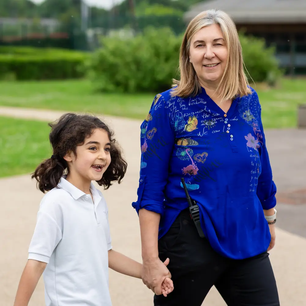 A young girl at Luxborough Court School walking with a teacher outside
