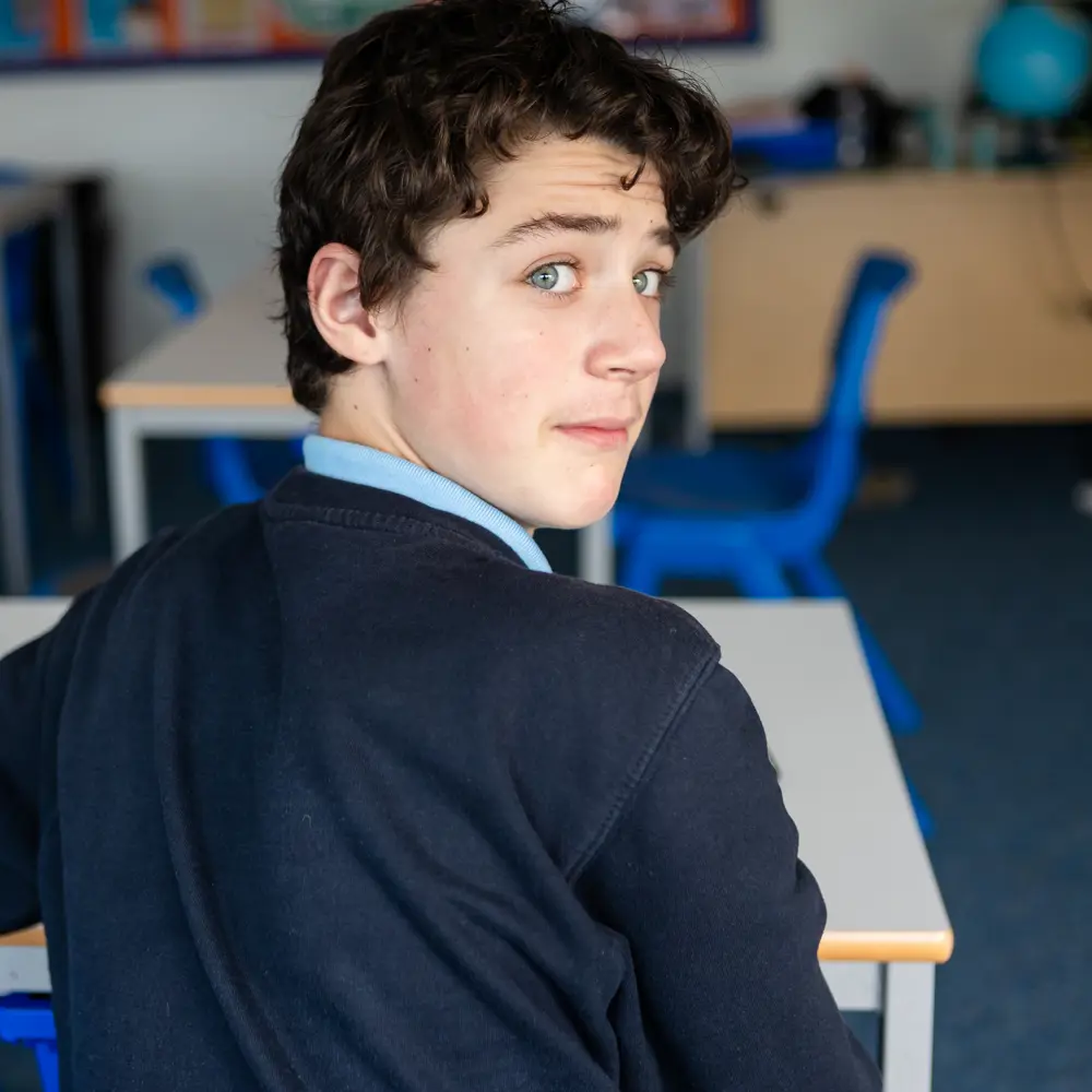 A young boy from Queensmead House School sitting at a desk turning round to look at the camera