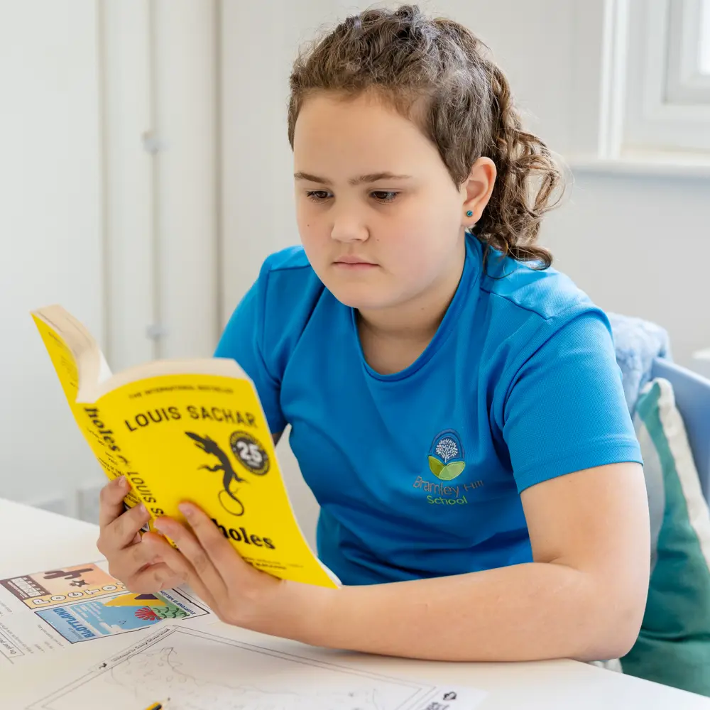 A young girl wearing a pony tail at Bramley Hill School reading a book in a classroom