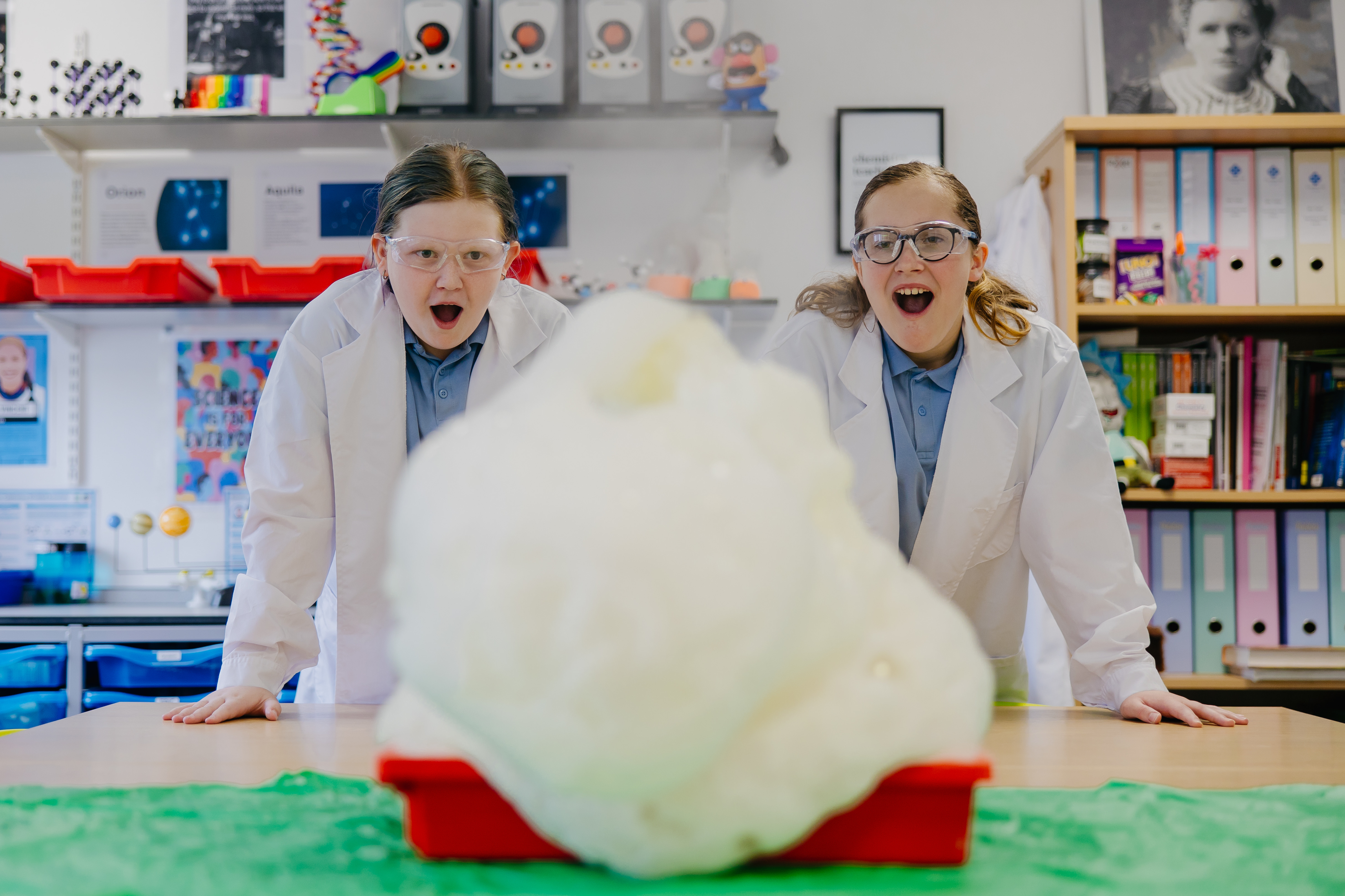 To girls either side of a tall mountain of foam from a science experiment 