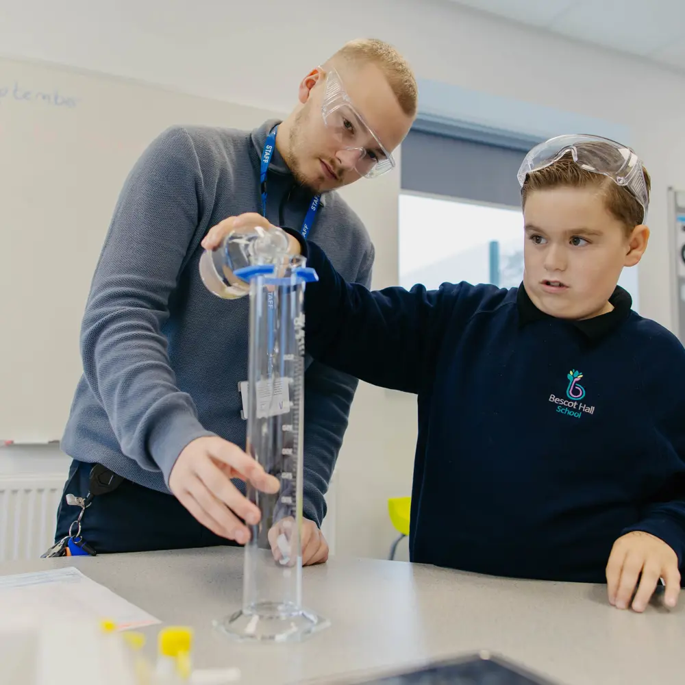 A young boy at Bescot Hall School pouring a solution into a beaker with the help of a teacher