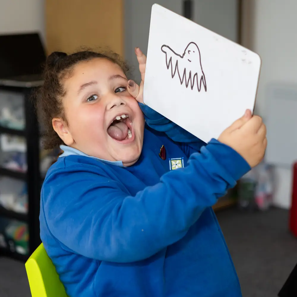 Young pupil happy and smiling at Hinckley House School while holding a whiteboard with a drawing of a ghost