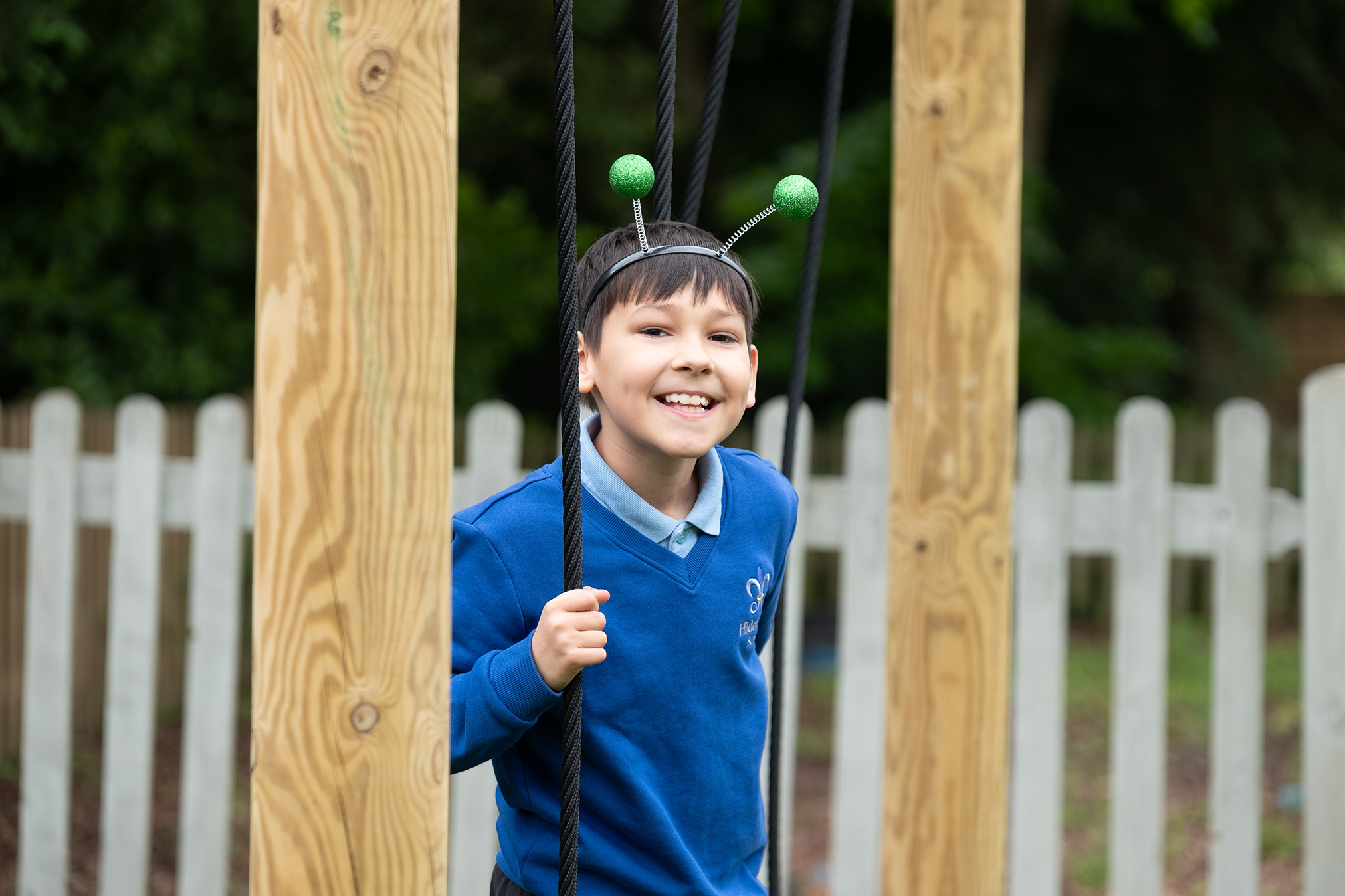 A young boy smiling on a swing set at Hilden Park School