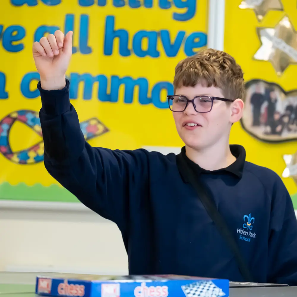 A young boy with brown hair and glasses from Hilden Park School raising his hand