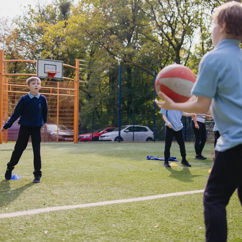 Two young boys in blue school uniform playing catch on a sports pitch