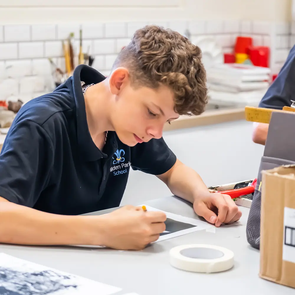 A boy sitting in an art classroom drawing with a pencil