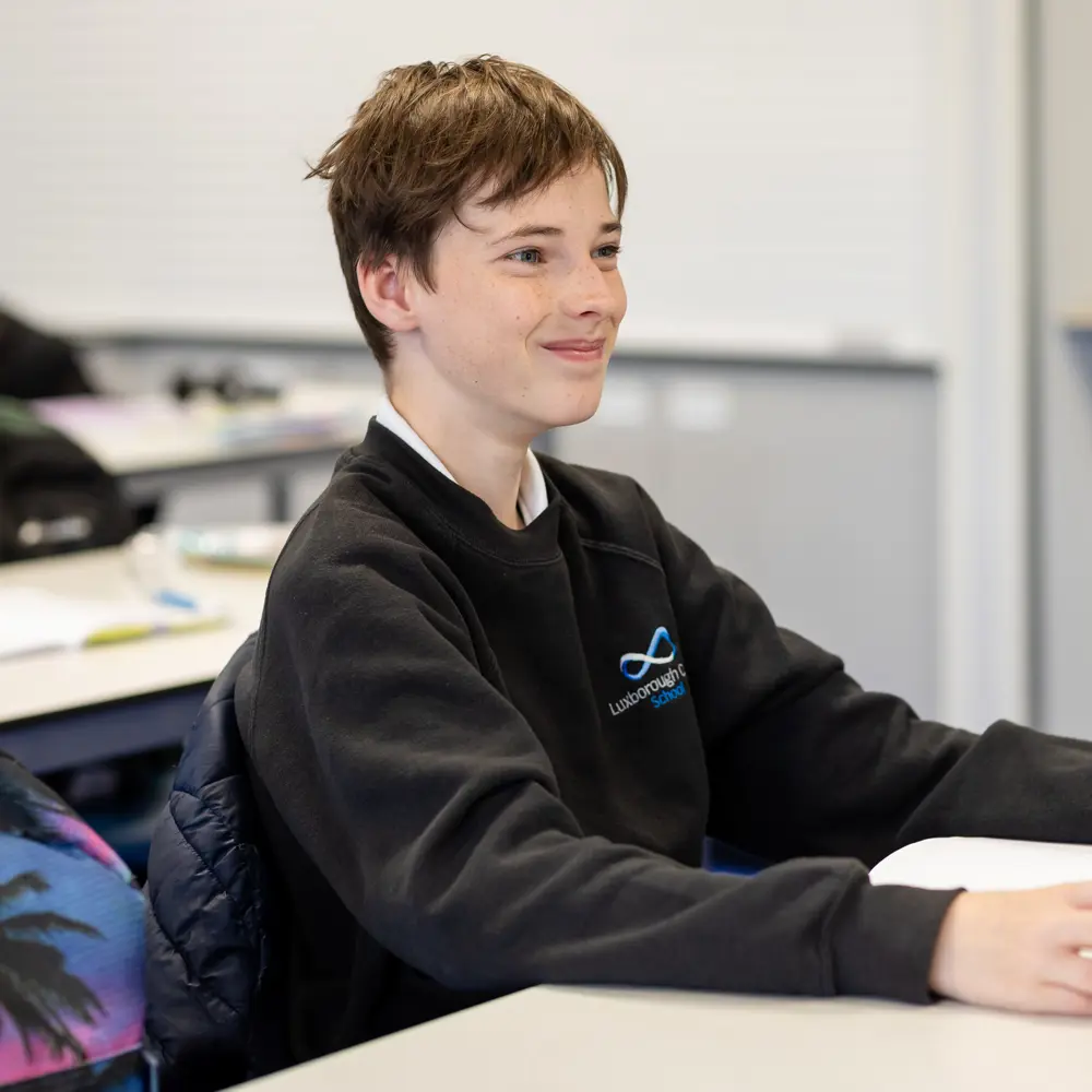 A young boy with brown hair at Luxborough Court School sitting at a desk smiling