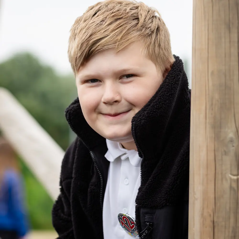 Young boy from Luxborough Court School sat on playing frame smiling at camera