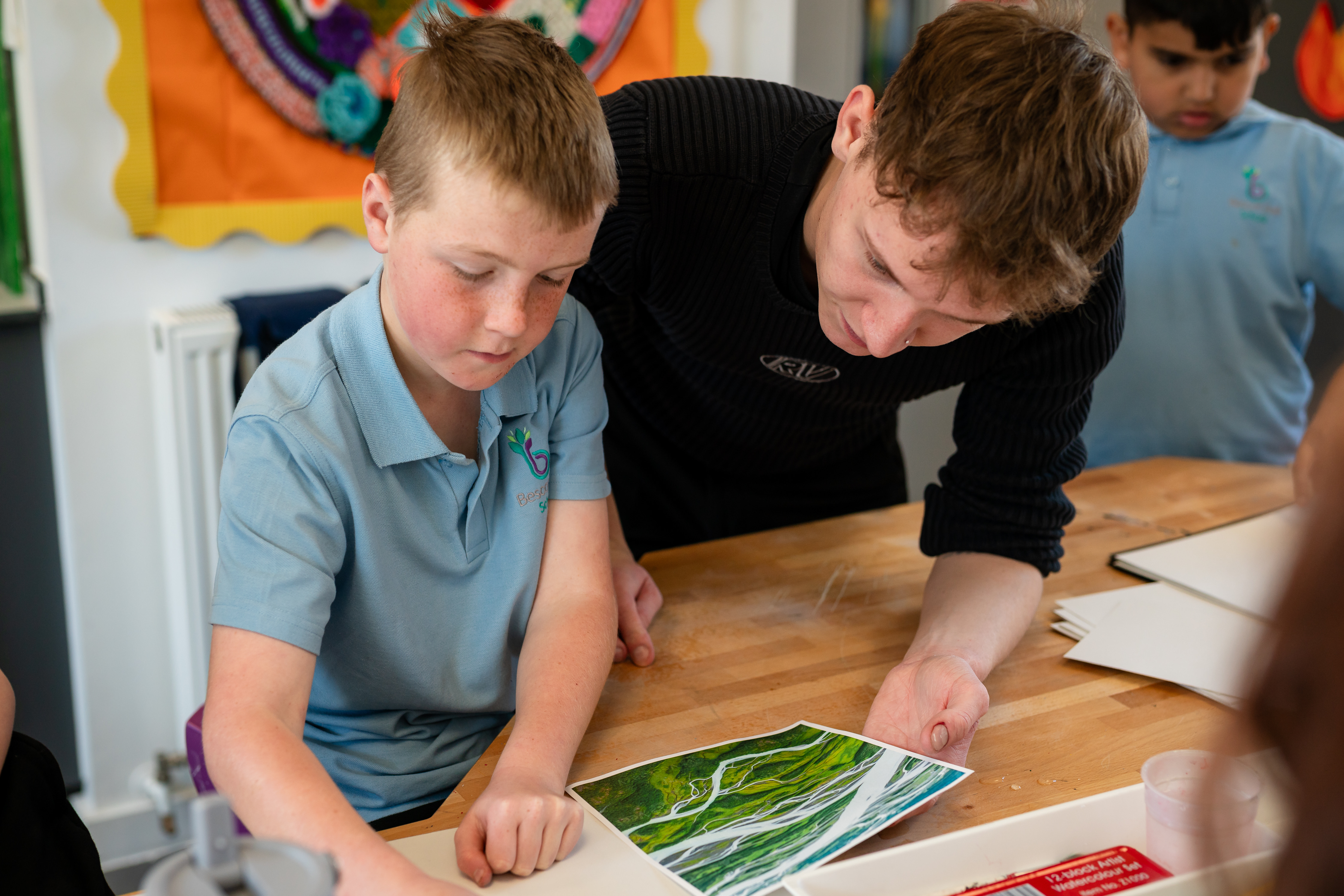 Staff memeber helping student with art in a classroom