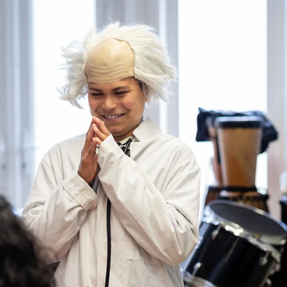 A young boy from Greenholm School smiling whilst dressing up in a white lab coat and wig