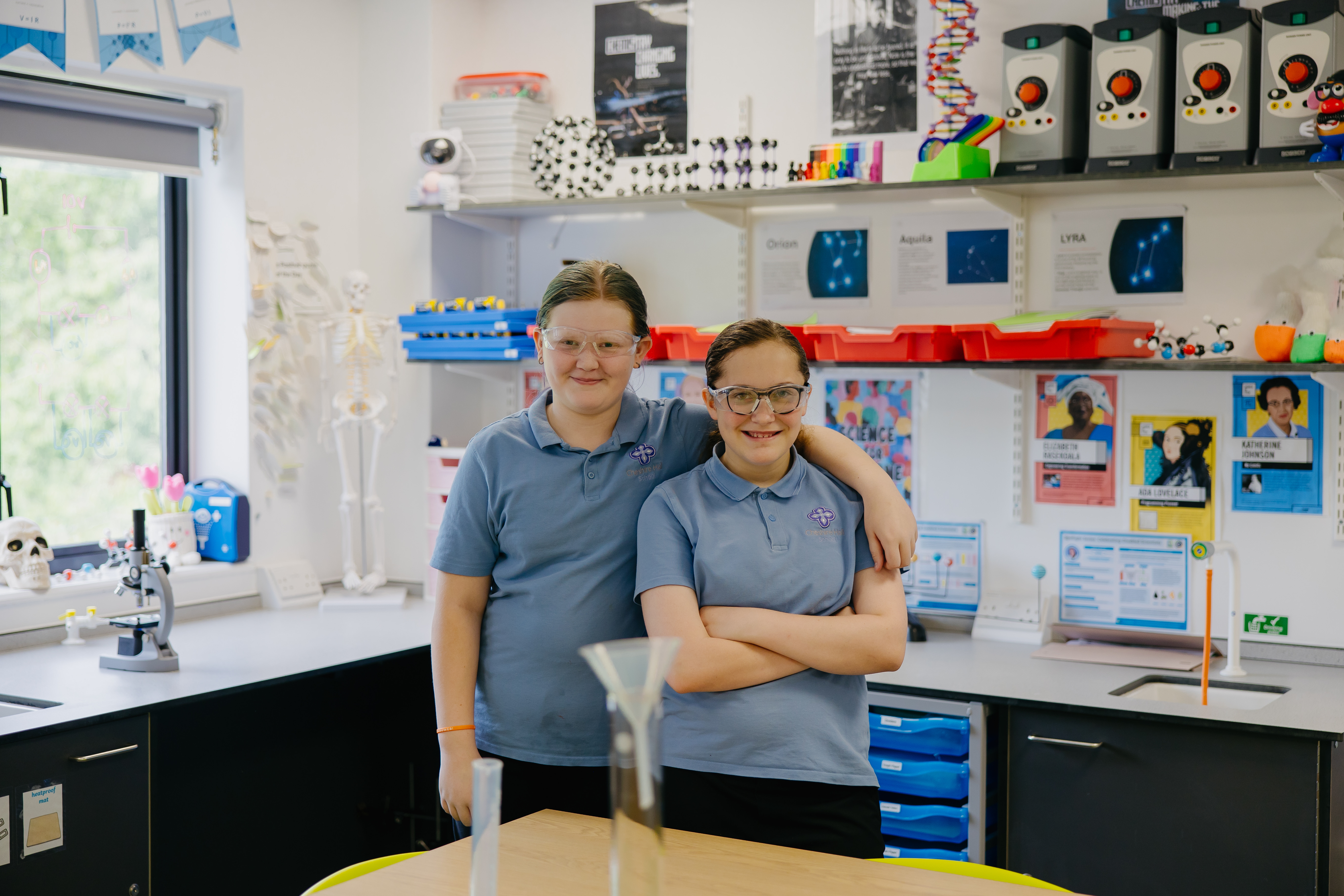 Two girls stood in classroom with arms round eachother