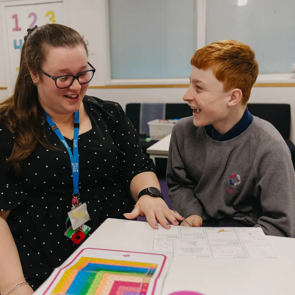 Young boy and member of staff sat at a desk at Bridgeway School learning