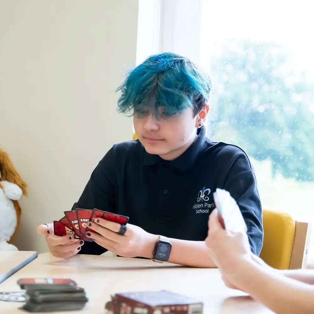 A young boy at Hilden Park School with blue hair playing a card game with peers