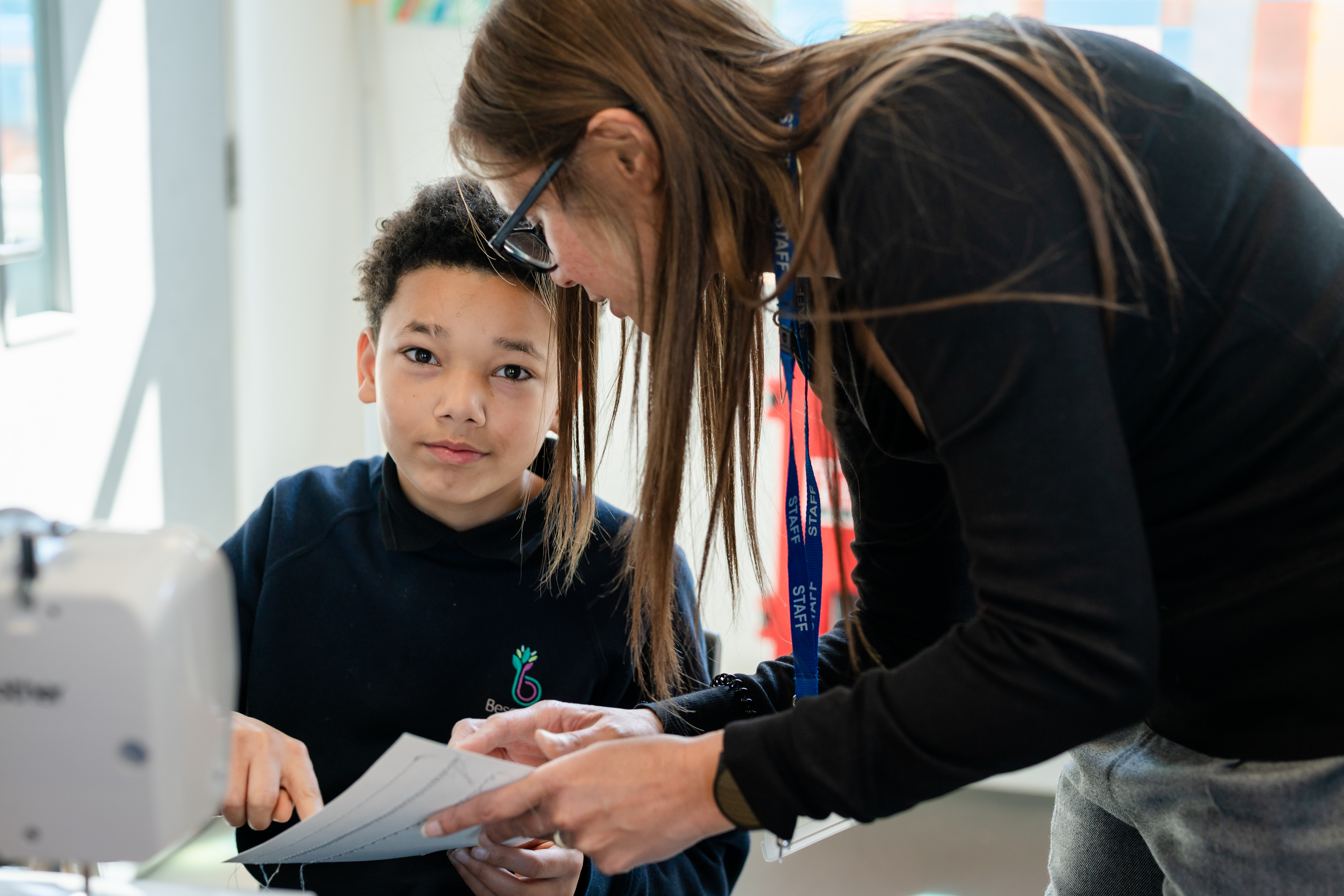 Boy looking at camera smiling as teacher stands next to him teaching