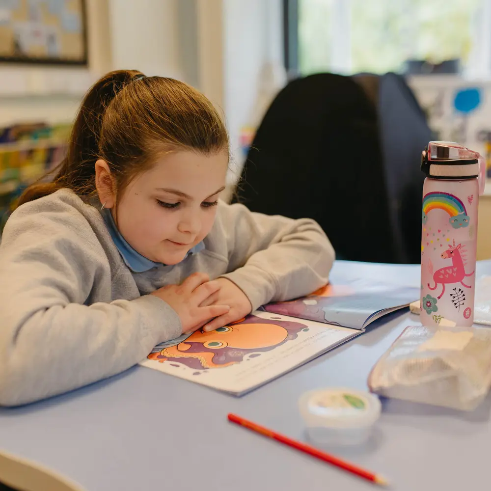 A young girl sitting at a desk reading a book at Cedar House School