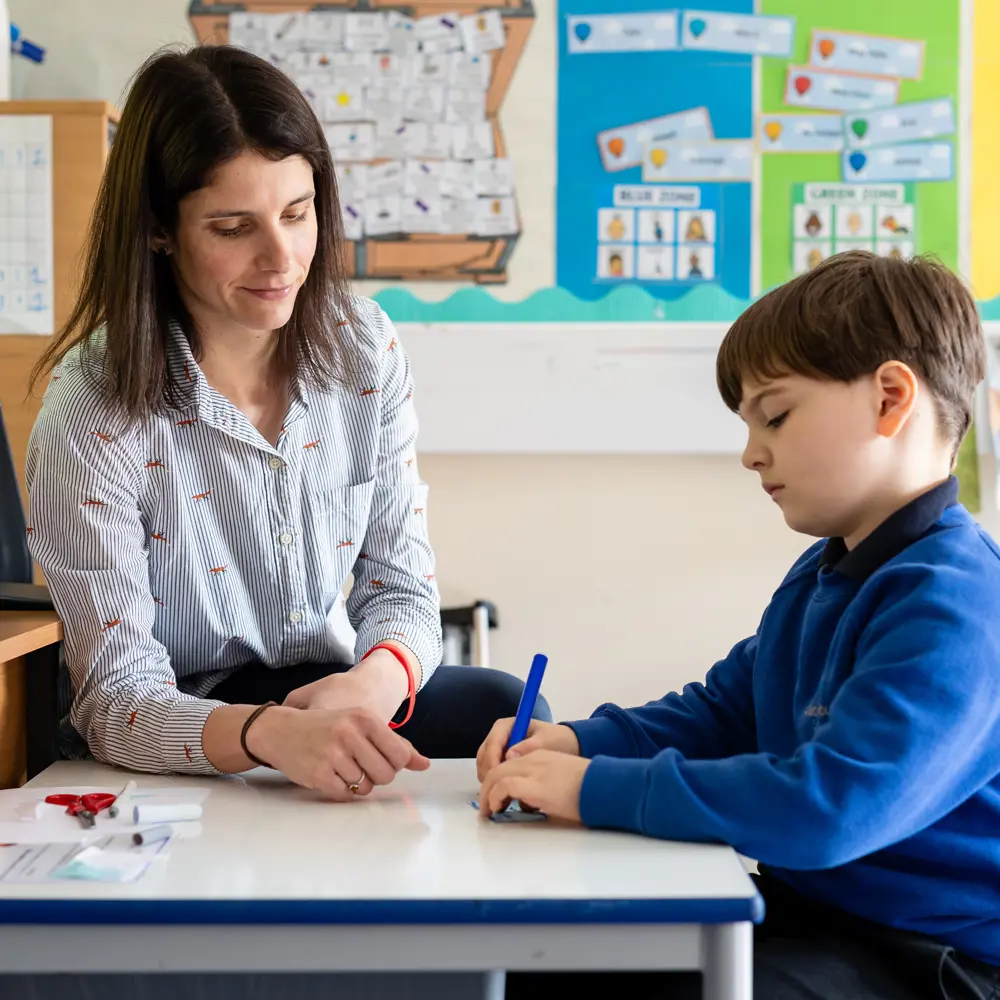 Young boy with member of staff sat at a desk learning