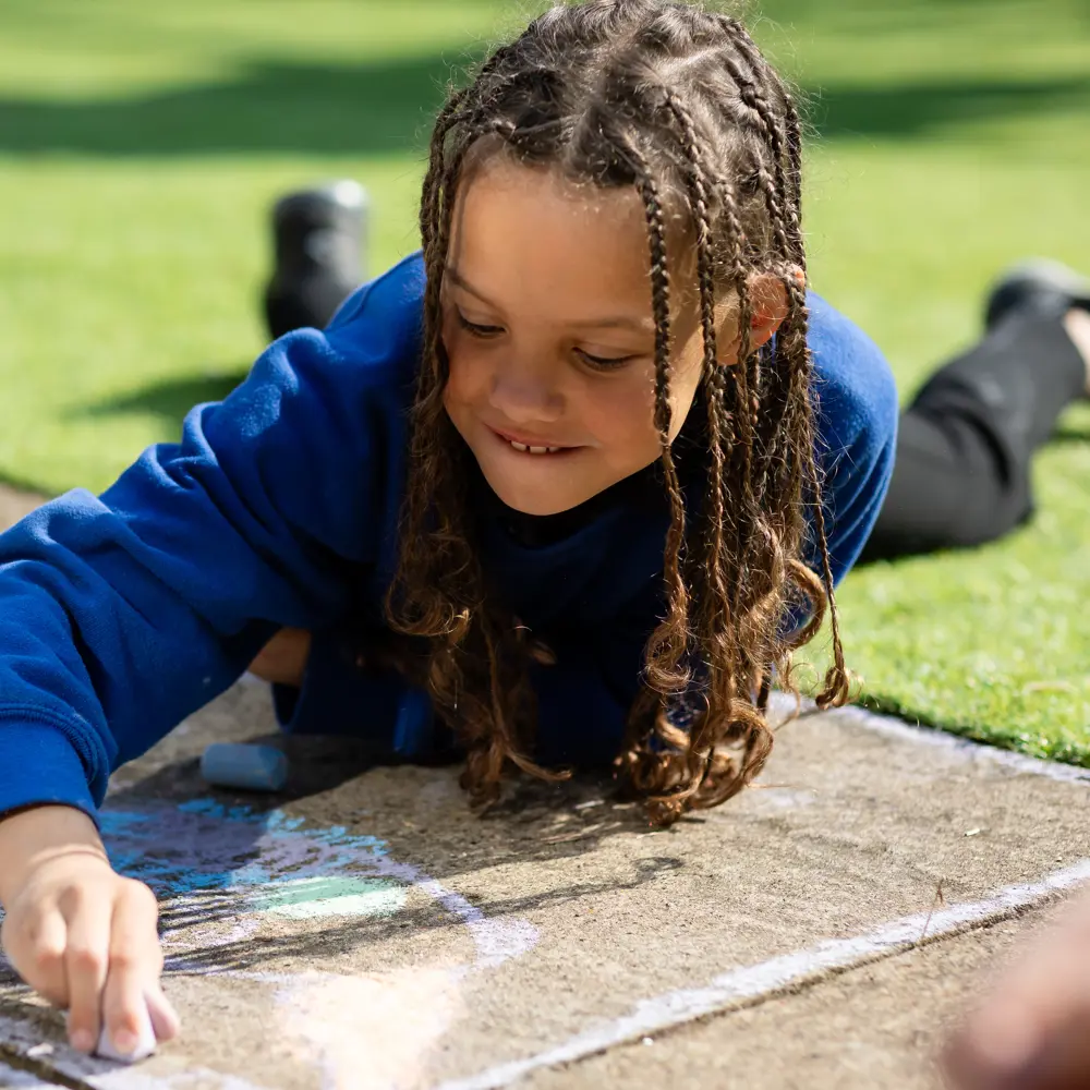 Girl from Chilworth House School lying down outside drawing with chalk