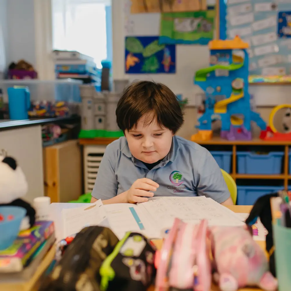 A young boy from Cedar House School reading a book in a classroom