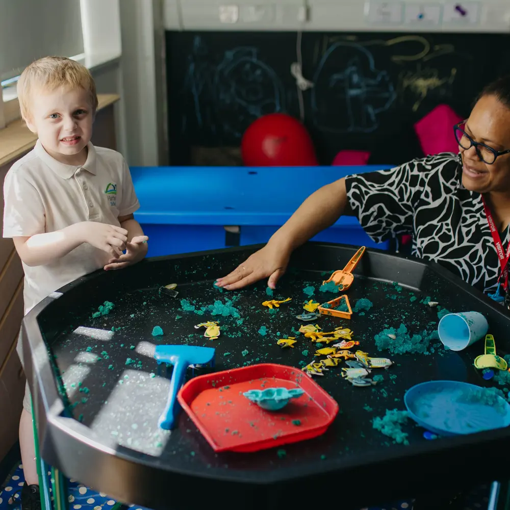 Young boy and teacher from Hartwell School playing with sand and toys in a classroom