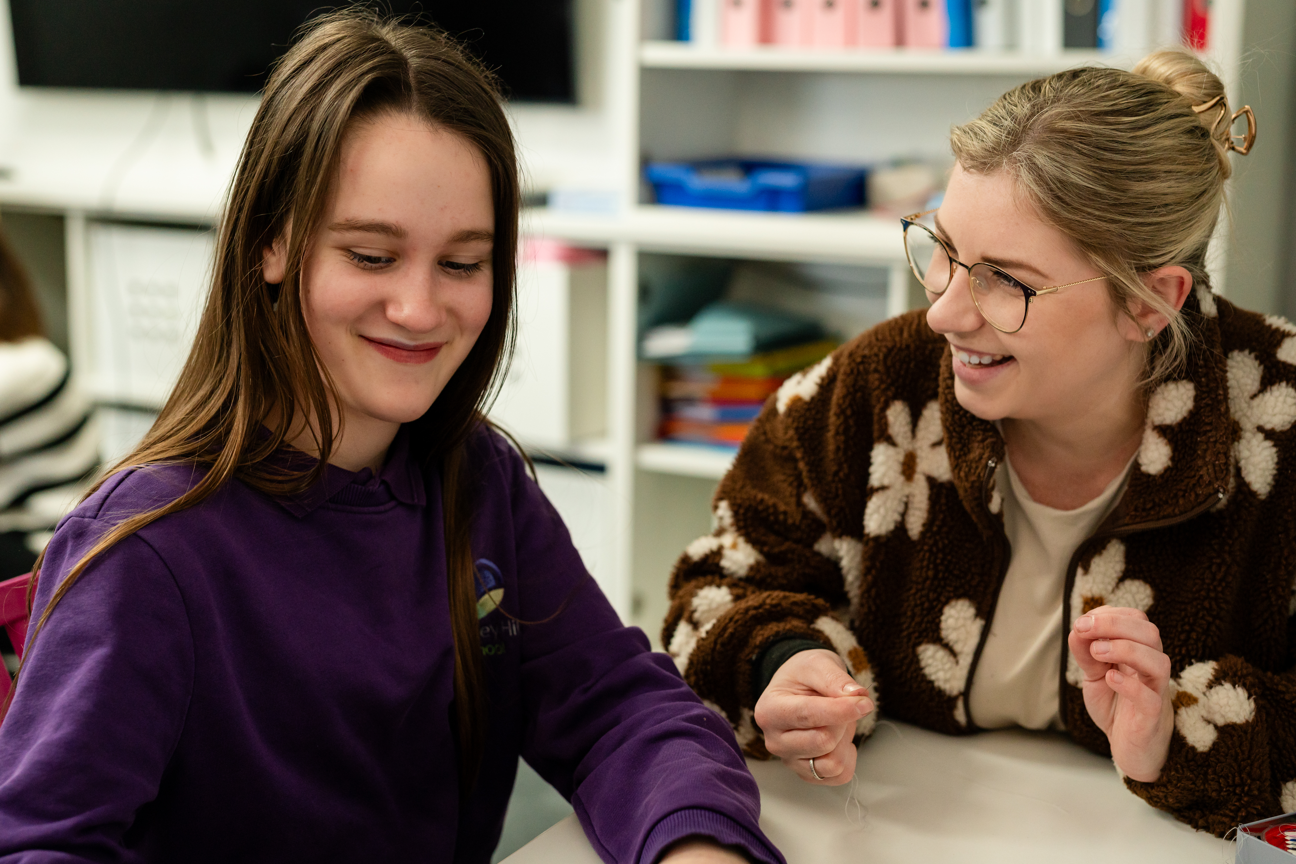 Pupil and teacher smiling at school desk