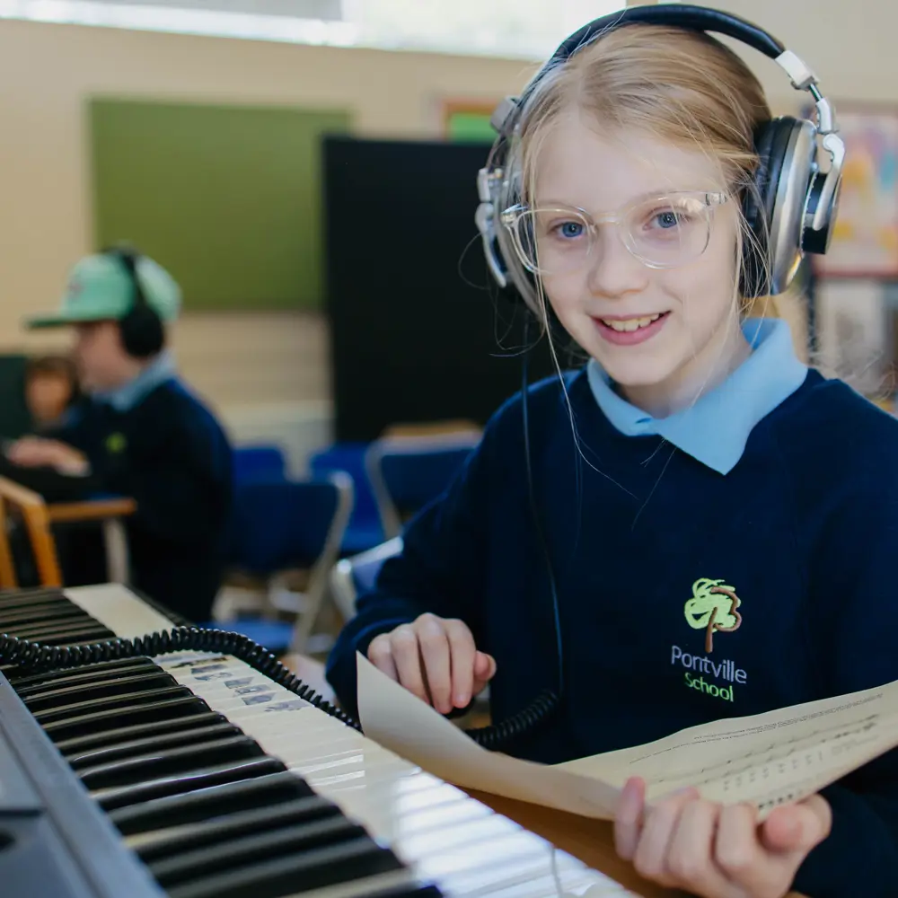 Young girl from Pontville School wearing headphones while playing the piano