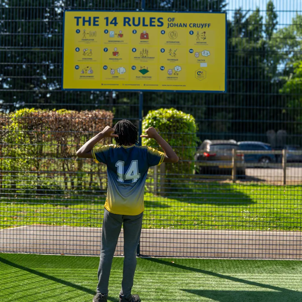 A young boy at Chilworth House Upper School on the cruyff court pointing to the number 14 on the back of his shirt