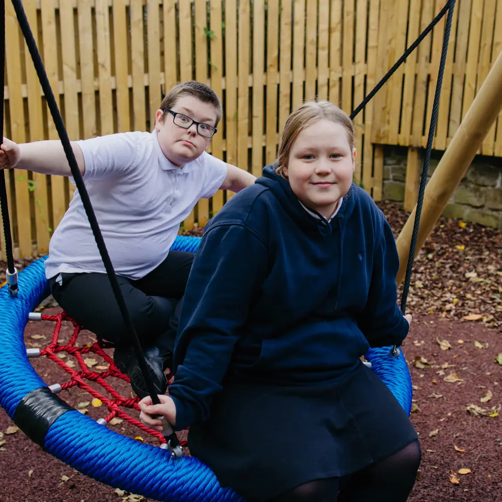 Two pupils at Millcourt School playing on the basket swing outside
