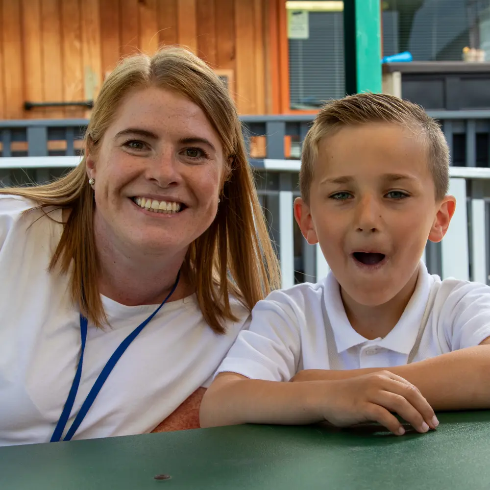 A young boy at Lakeside School sitting with a staff member looking at the camera
