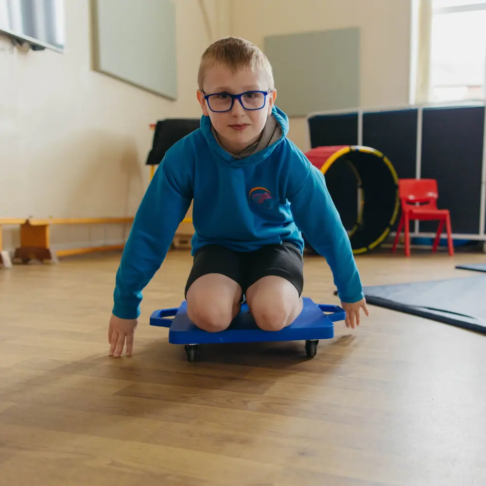 A young boy at Westmorland School in the sports hall kneeling on a balance board